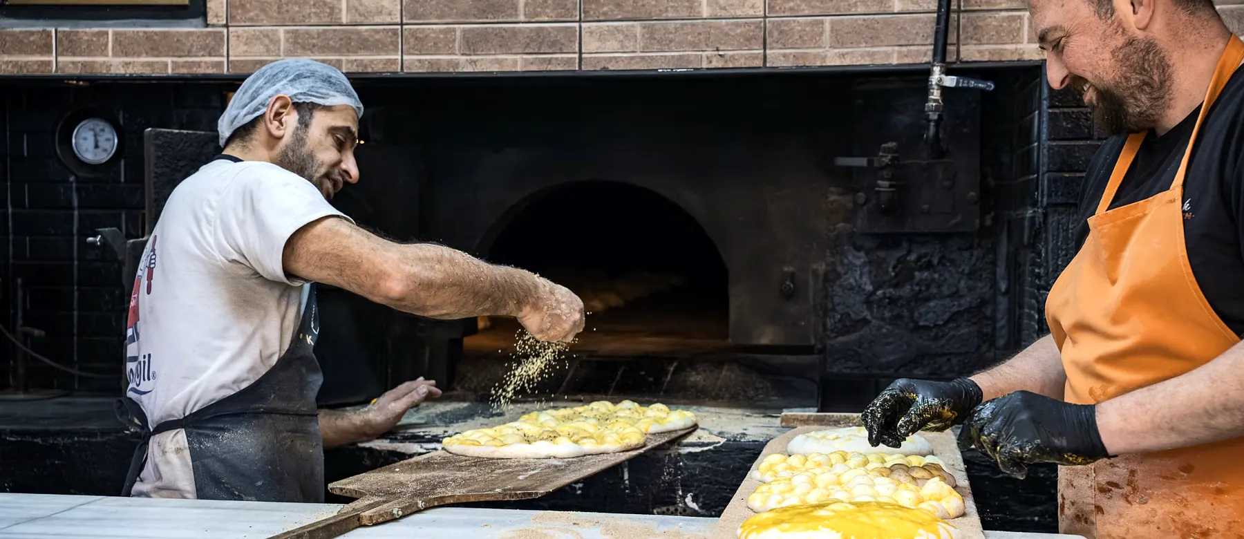 Bakers preparing flatbreads beside a brick oven
