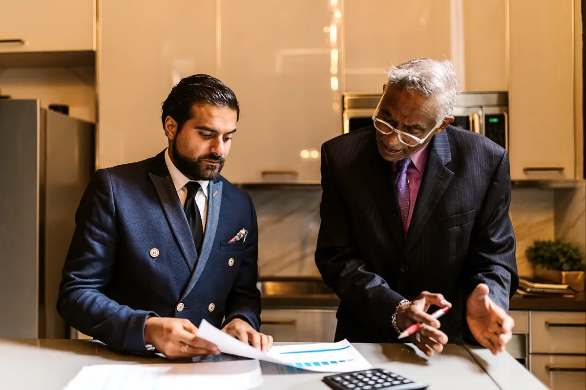Two men reviewing printed documents and a calculator at a counter
