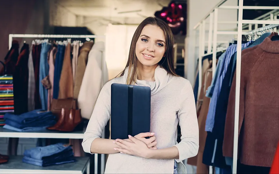 Boutique owner holding a folder among clothing racks in her shop