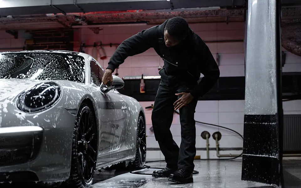 Car wash attendant washing a soaped car in a wash bay