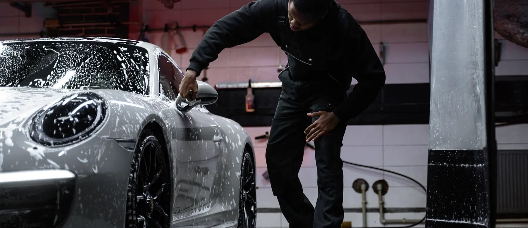 Car wash attendant washing a soaped car in a wash bay