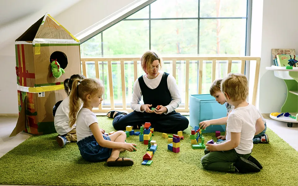 Teacher playing with young children on the floor of a bright classroom