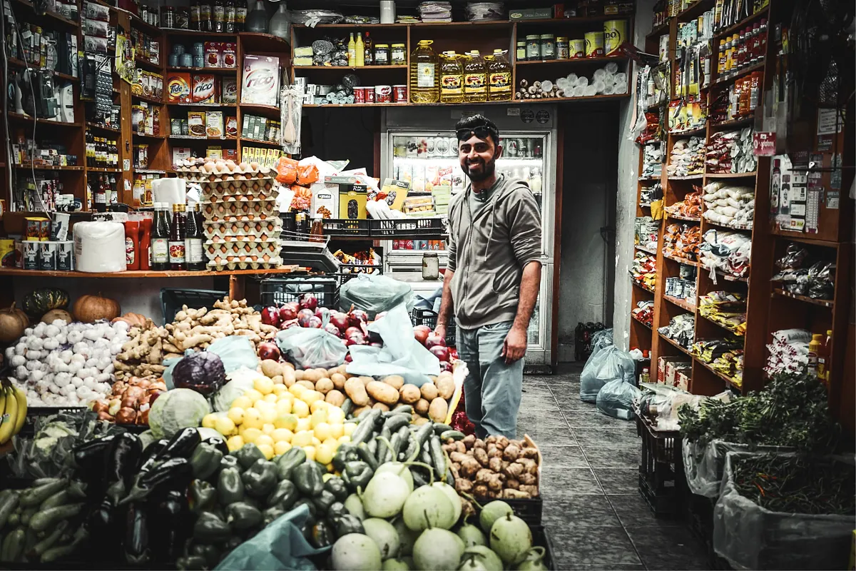 Grocer standing among fresh produce and stocked shelves in his store