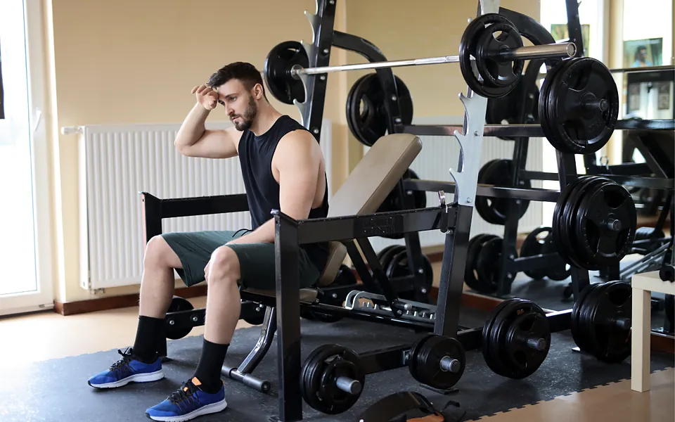 Gym member resting on a bench beside weight racks