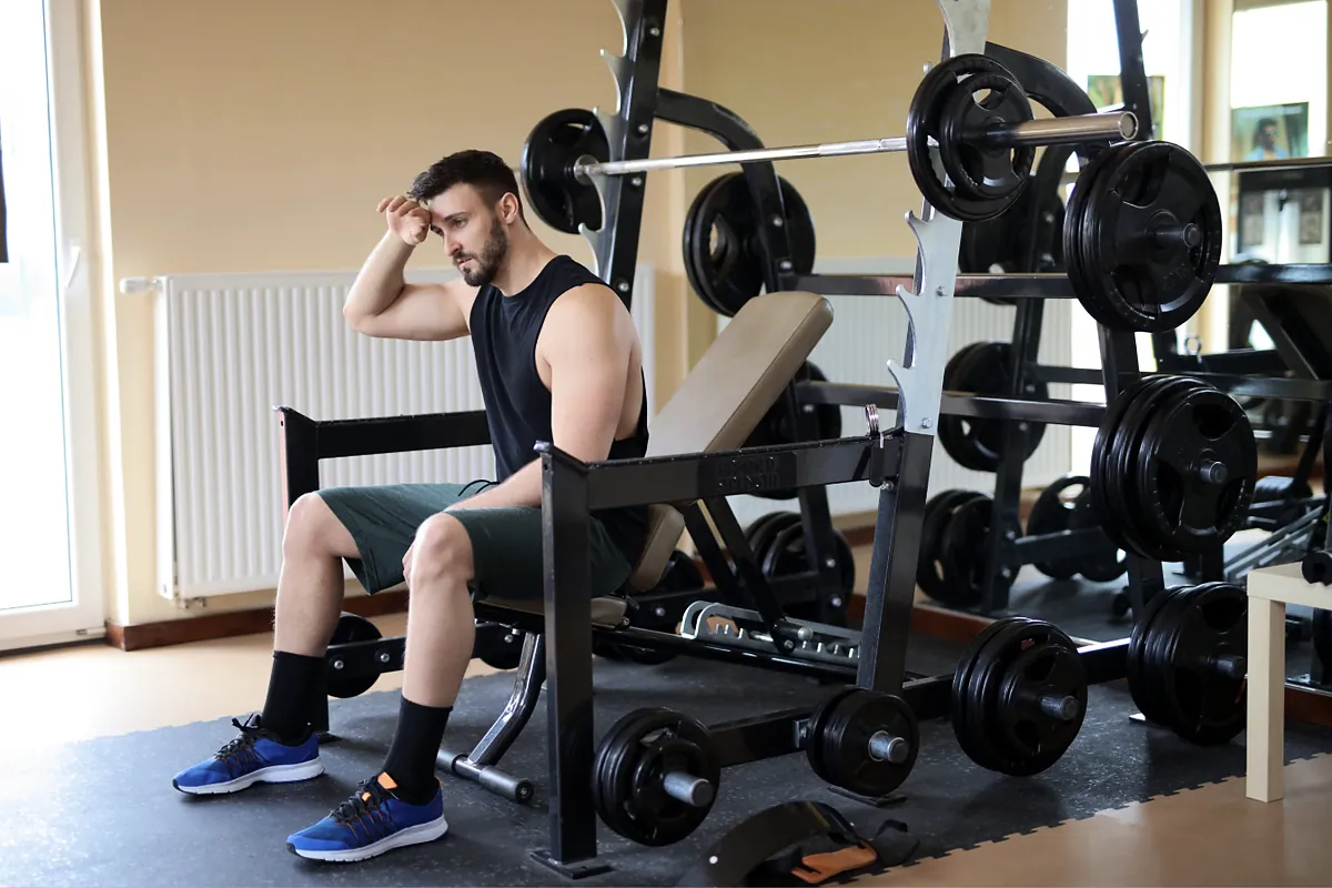 Gym member resting on a bench beside weight racks