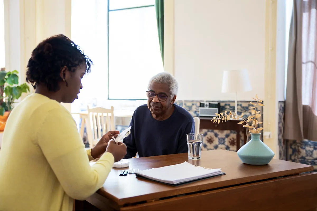 Home care aide reviewing paperwork with an older man at his kitchen table