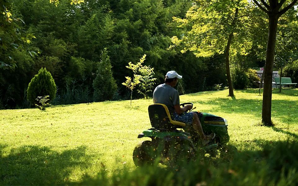 Landscaper on a riding mower cutting a sunny lawn