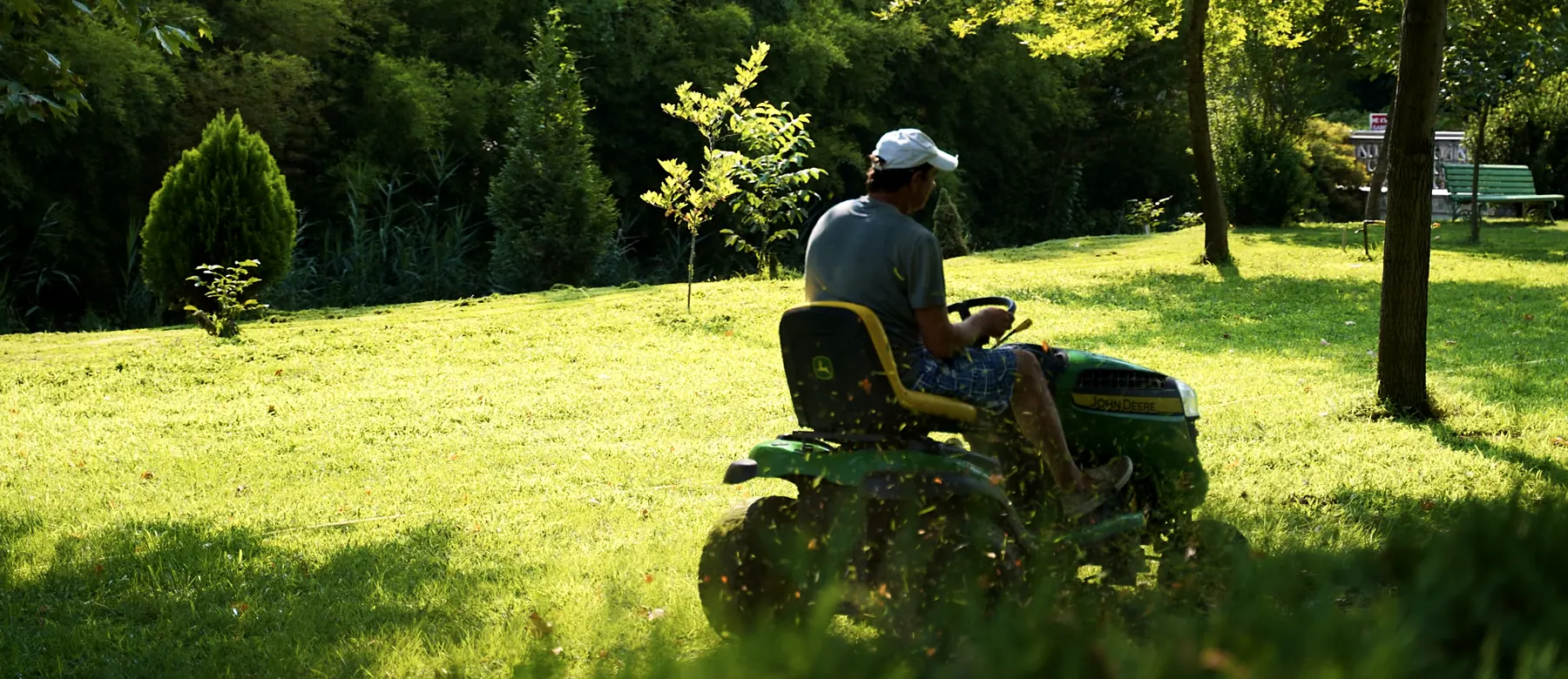 Landscaper on a riding mower cutting a sunny lawn