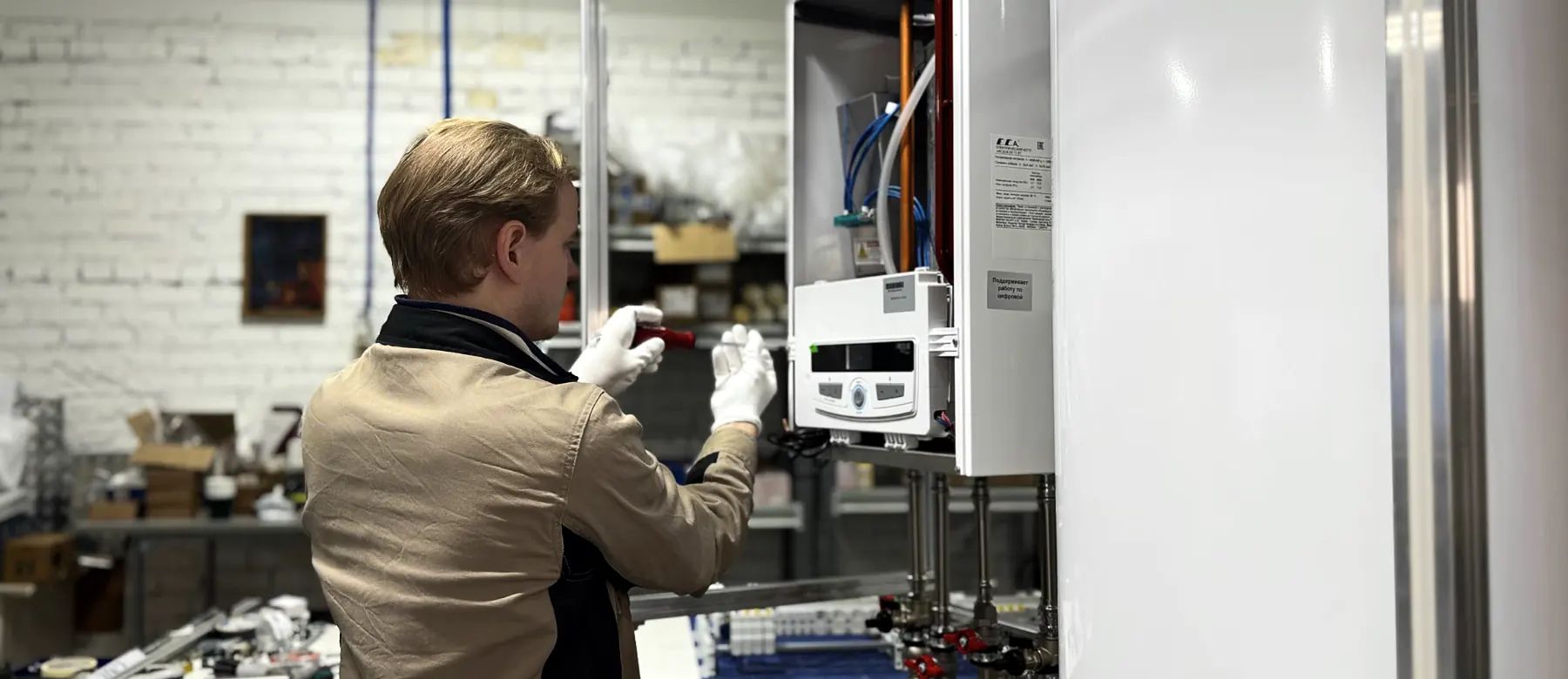 Technician installing a wall mounted boiler and water lines in a workshop