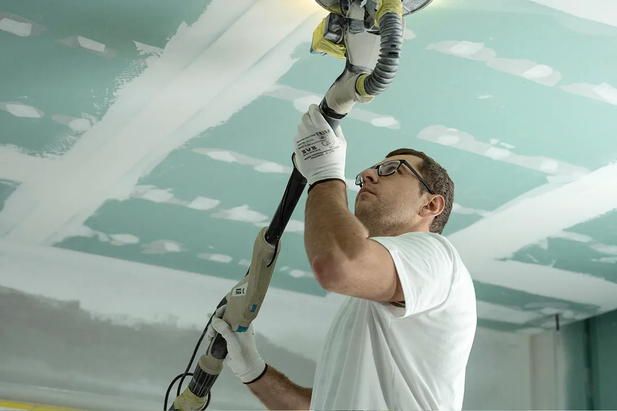 Contractor sanding a repaired drywall ceiling during a home rebuild