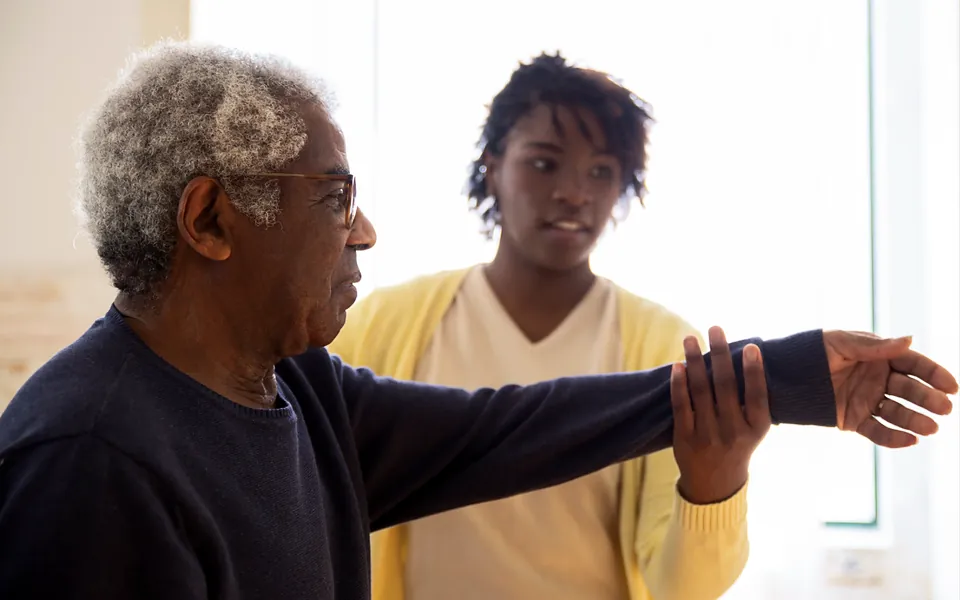 Caregiver helping an older man with an arm exercise