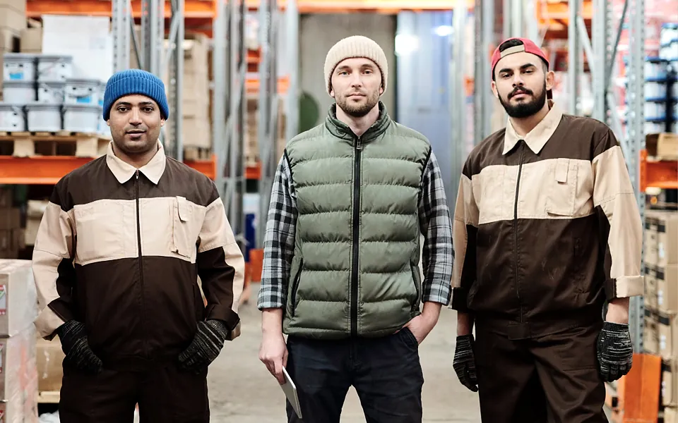 Three warehouse workers in work clothes standing in a stocked aisle