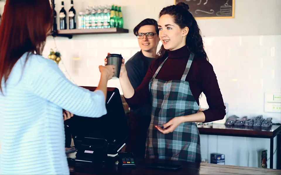 Café owner in a plaid apron serving a customer at the register