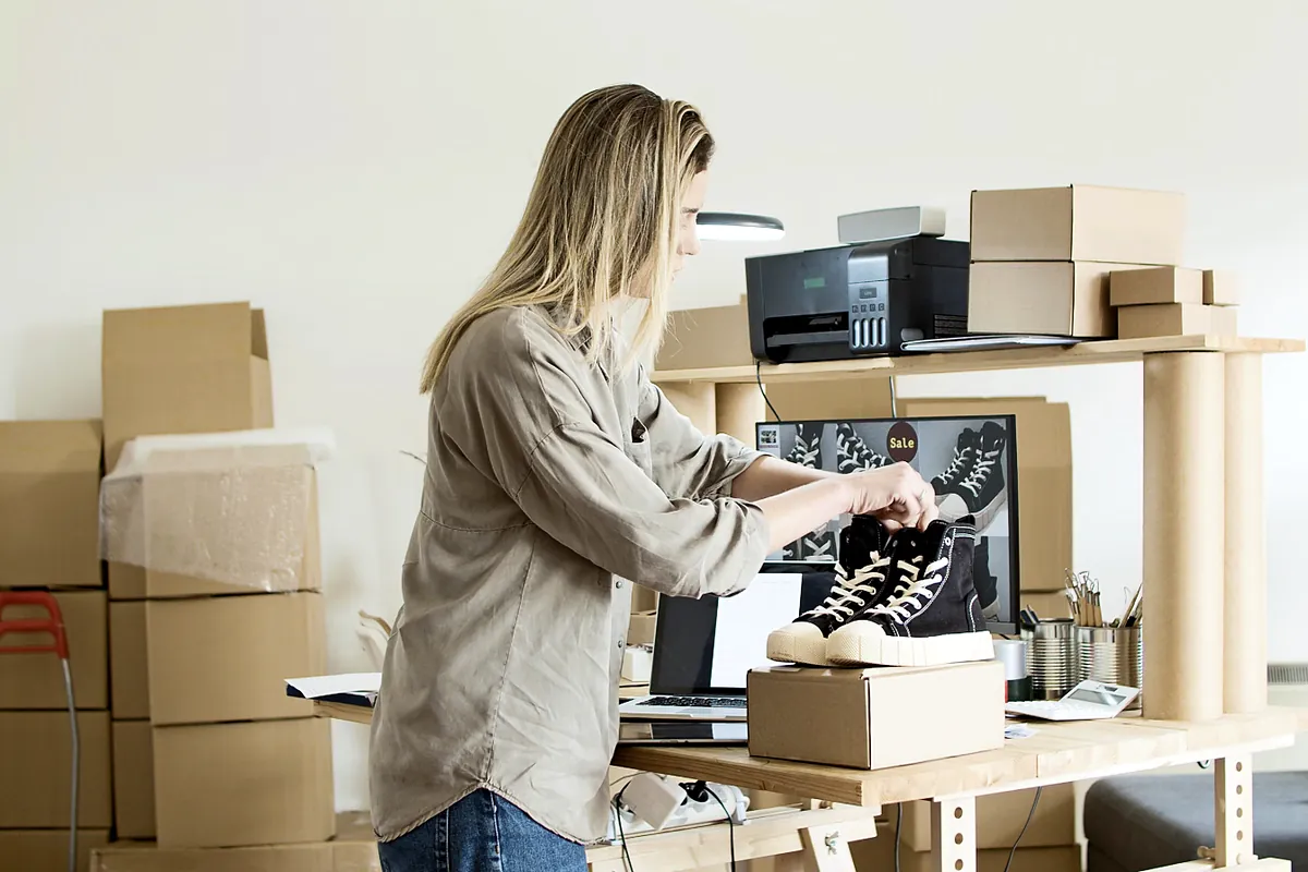 Online seller packing a pair of sneakers into a shipping box at her workspace